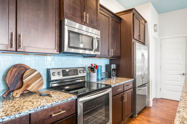 kitchen featuring backsplash, light stone countertops, dark brown cabinetry, light wood-type flooring, and appliances with stainless steel finishes