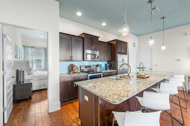 kitchen with a center island with sink, dark wood-type flooring, sink, decorative light fixtures, and stainless steel appliances