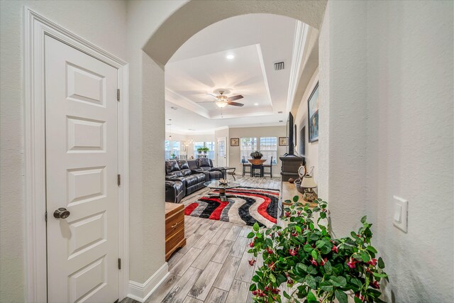 interior space with light wood-type flooring, a raised ceiling, and crown molding