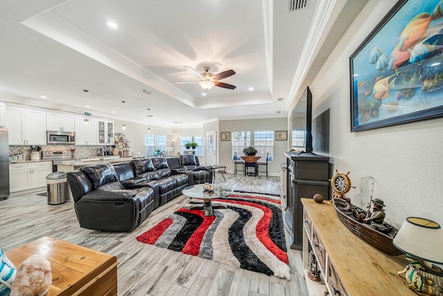 living room with ceiling fan, a raised ceiling, light wood-type flooring, and crown molding