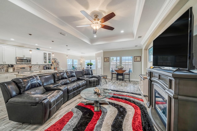 living room featuring ceiling fan, light hardwood / wood-style flooring, ornamental molding, and a tray ceiling