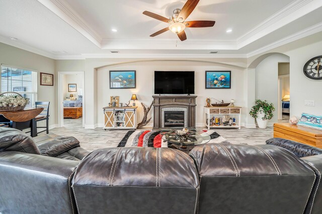 living room with light wood-type flooring, a tray ceiling, ceiling fan, and crown molding