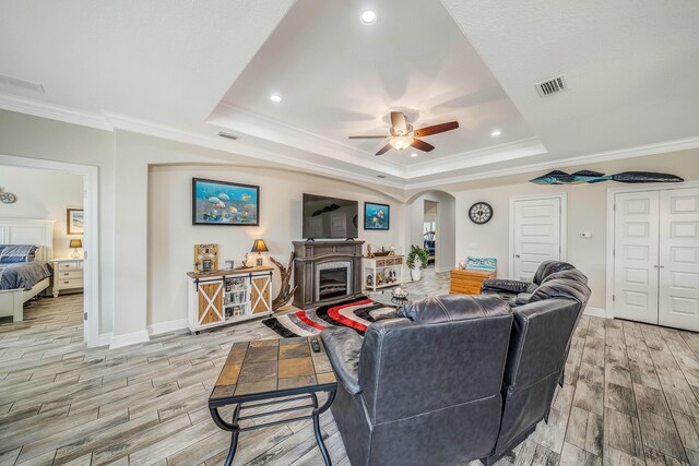 living room with light wood-type flooring, a tray ceiling, ceiling fan, and crown molding