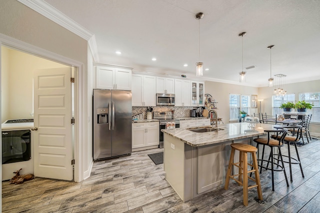 kitchen with pendant lighting, sink, a kitchen island with sink, stainless steel appliances, and washer / dryer