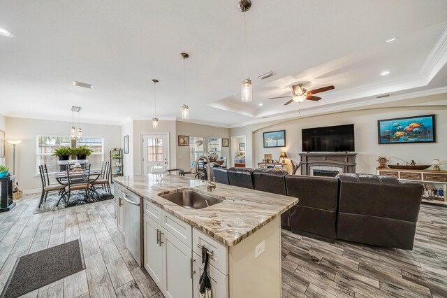 kitchen with light stone counters, a kitchen island with sink, sink, ceiling fan with notable chandelier, and hanging light fixtures