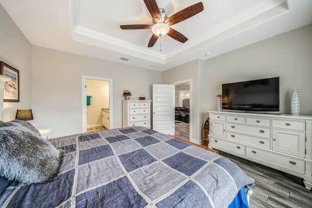 bedroom featuring ceiling fan, a raised ceiling, ensuite bathroom, and wood-type flooring