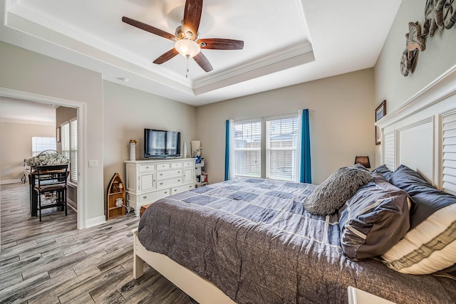 bedroom featuring ceiling fan, a tray ceiling, ornamental molding, and light hardwood / wood-style flooring