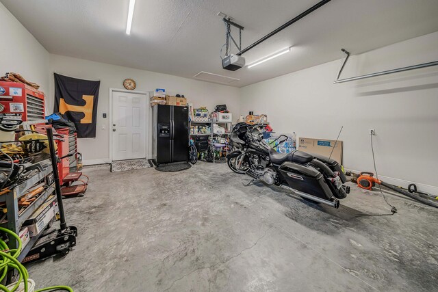 garage featuring a garage door opener and black fridge with ice dispenser