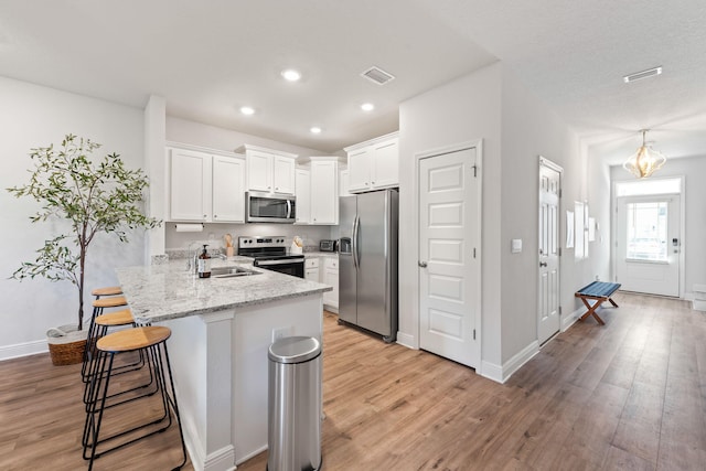 kitchen featuring a breakfast bar, white cabinets, kitchen peninsula, light hardwood / wood-style flooring, and stainless steel appliances