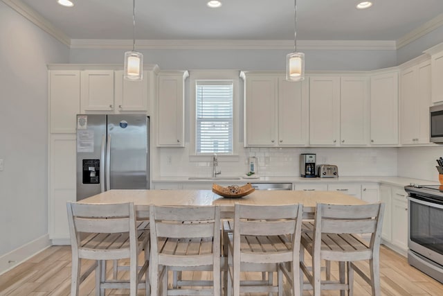 kitchen with appliances with stainless steel finishes, hanging light fixtures, sink, and light hardwood / wood-style flooring