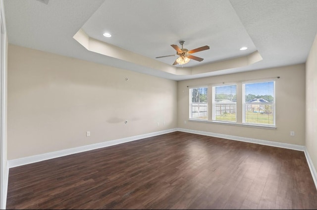 unfurnished room with a textured ceiling, a raised ceiling, dark hardwood / wood-style floors, and ceiling fan