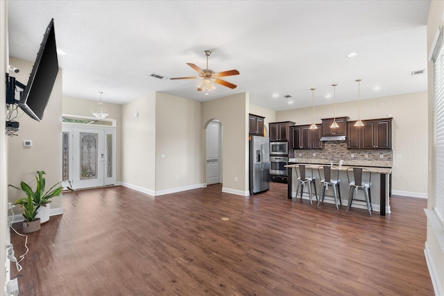 kitchen with dark wood-type flooring, a kitchen bar, hanging light fixtures, and a kitchen island with sink