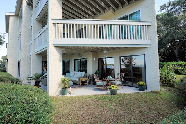 back of property featuring a balcony, a patio, an outdoor hangout area, and a lawn