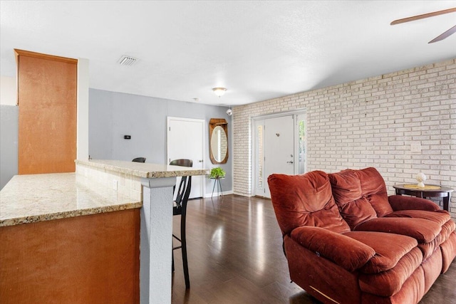 living room with dark wood-type flooring, ceiling fan, and brick wall