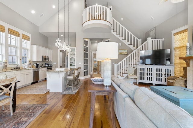 living room with a notable chandelier, built in features, light hardwood / wood-style floors, and high vaulted ceiling