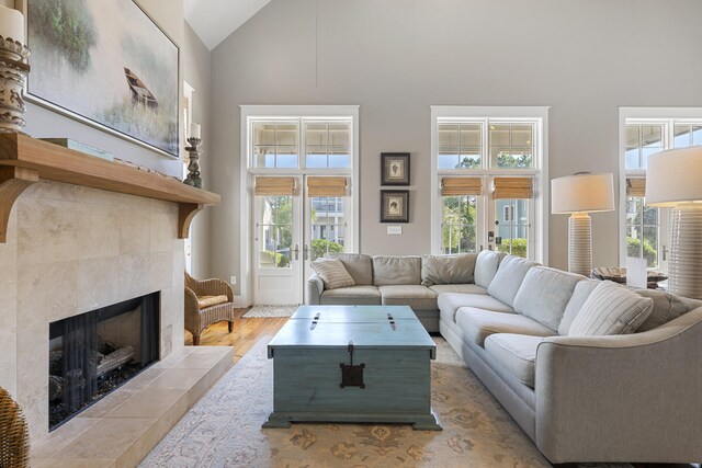 living room featuring high vaulted ceiling, light wood-type flooring, a fireplace, and french doors