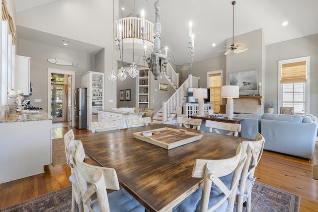 dining area with ceiling fan with notable chandelier, dark wood-type flooring, and high vaulted ceiling