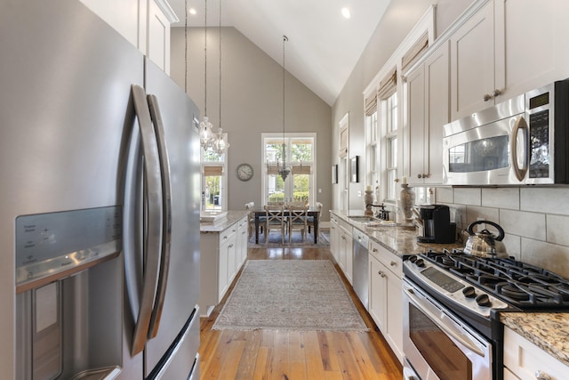 kitchen featuring light stone counters, decorative light fixtures, white cabinetry, appliances with stainless steel finishes, and light wood-type flooring