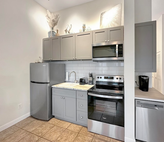 kitchen featuring decorative backsplash, light tile patterned floors, appliances with stainless steel finishes, gray cabinetry, and sink