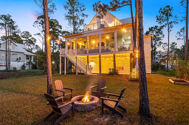 back house at dusk featuring a yard, ceiling fan, a balcony, and an outdoor fire pit