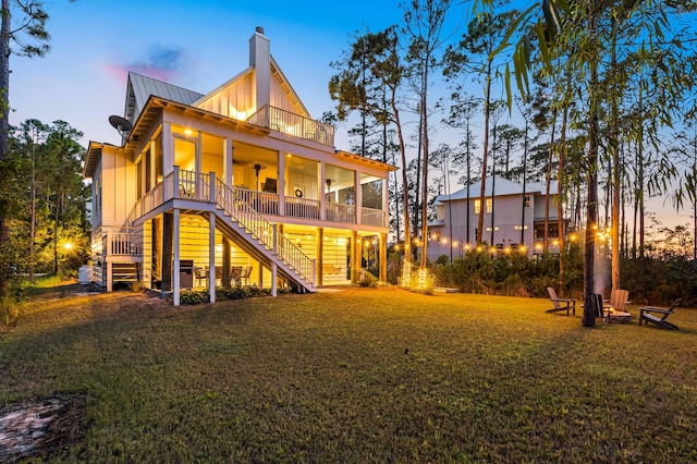 back house at dusk featuring a lawn, ceiling fan, and a balcony