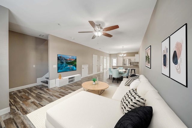 living area featuring stairway, wood finished floors, visible vents, baseboards, and ceiling fan with notable chandelier