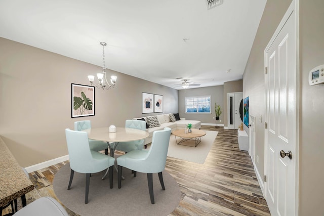 dining room featuring ceiling fan with notable chandelier, baseboards, wood finished floors, and visible vents