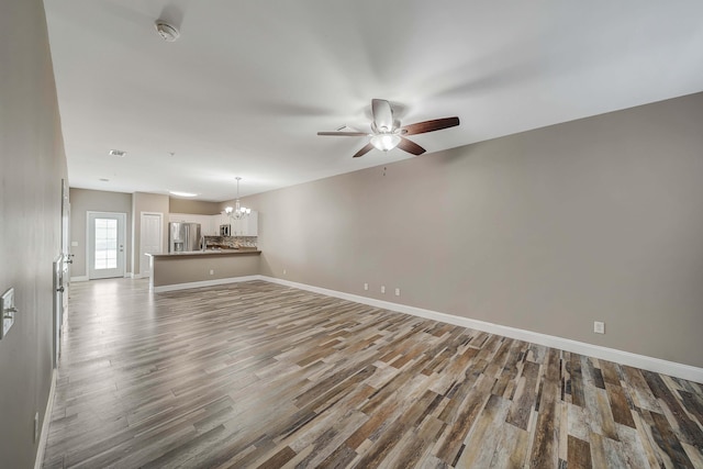 unfurnished living room with ceiling fan with notable chandelier, baseboards, wood finished floors, and visible vents