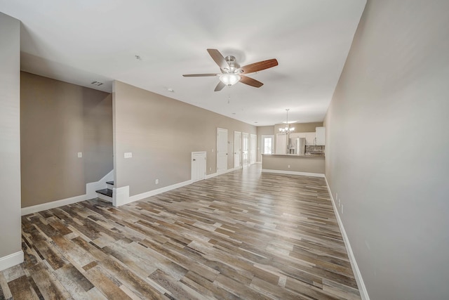 spare room featuring stairway, wood finished floors, ceiling fan with notable chandelier, baseboards, and visible vents