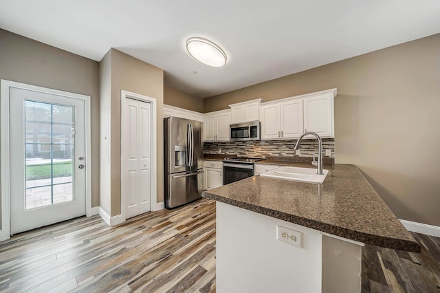 kitchen featuring stainless steel appliances, dark countertops, a sink, a peninsula, and white cabinetry
