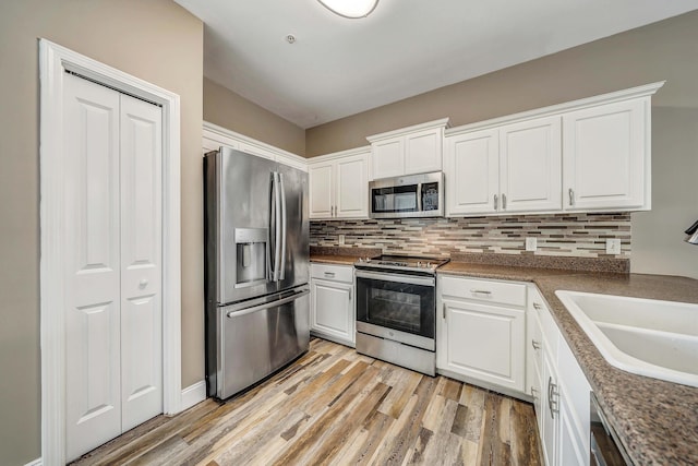 kitchen featuring light wood finished floors, stainless steel appliances, backsplash, a sink, and white cabinetry