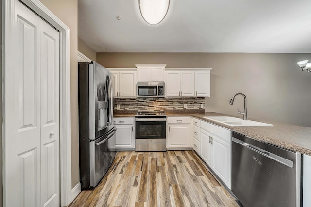kitchen featuring white cabinets, light wood finished floors, a sink, tasteful backsplash, and appliances with stainless steel finishes