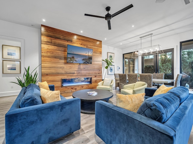 living room featuring ceiling fan with notable chandelier, light wood-type flooring, wood walls, and a fireplace