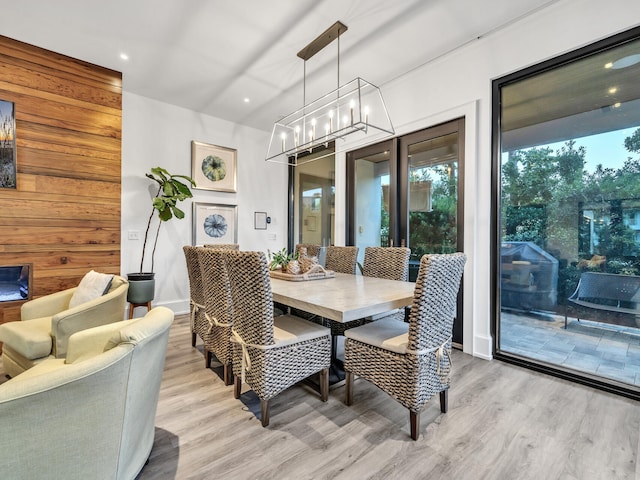 dining room with light hardwood / wood-style floors, wood walls, and an inviting chandelier