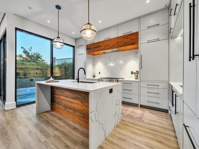 kitchen featuring light wood-type flooring, hanging light fixtures, a kitchen island with sink, and sink