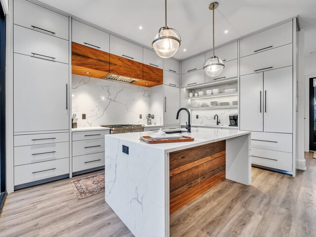 kitchen featuring light wood-type flooring, a center island with sink, backsplash, and pendant lighting