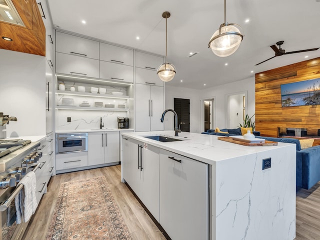 kitchen featuring an island with sink, decorative light fixtures, sink, and light hardwood / wood-style floors