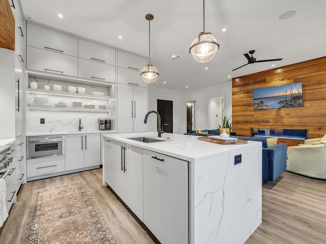 kitchen with sink, decorative light fixtures, a center island with sink, white cabinetry, and light hardwood / wood-style floors