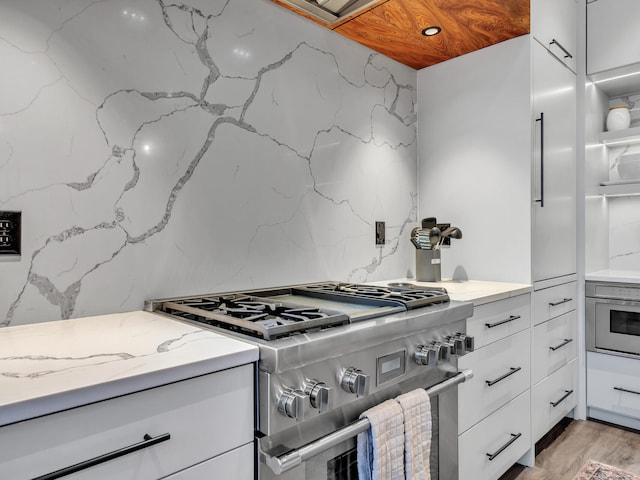 kitchen with light wood-type flooring, white cabinets, light stone counters, and stainless steel range