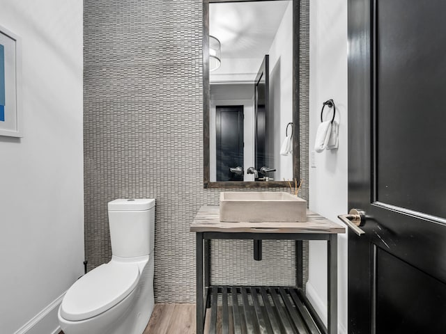 bathroom featuring wood-type flooring, tile walls, toilet, and sink