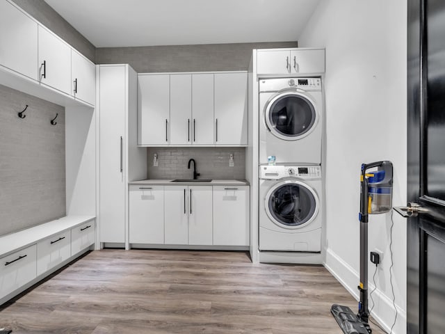 washroom with cabinets, light wood-type flooring, stacked washer / dryer, and sink