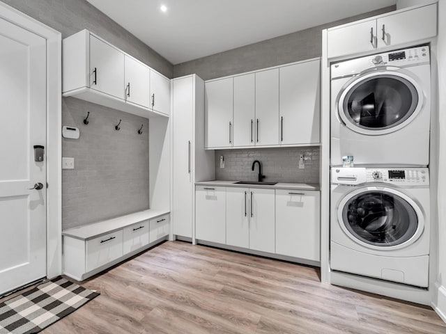 laundry area featuring light hardwood / wood-style floors, stacked washing maching and dryer, sink, and cabinets