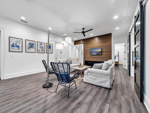 living room with wooden walls, ceiling fan, hardwood / wood-style flooring, and a barn door