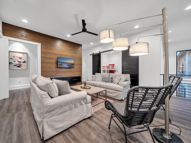 living room with wood walls, ceiling fan, hardwood / wood-style flooring, and a barn door