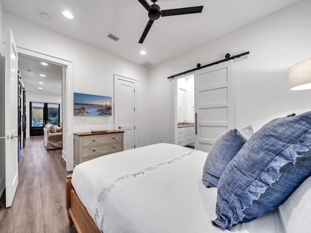 bedroom featuring a barn door, wood-type flooring, ensuite bath, and ceiling fan