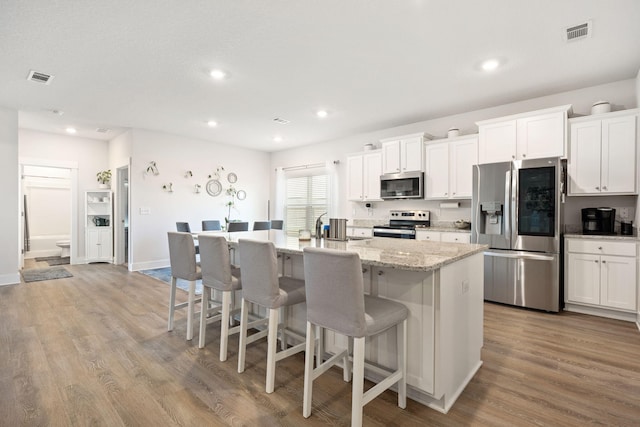 kitchen with appliances with stainless steel finishes, wood-type flooring, an island with sink, and white cabinets