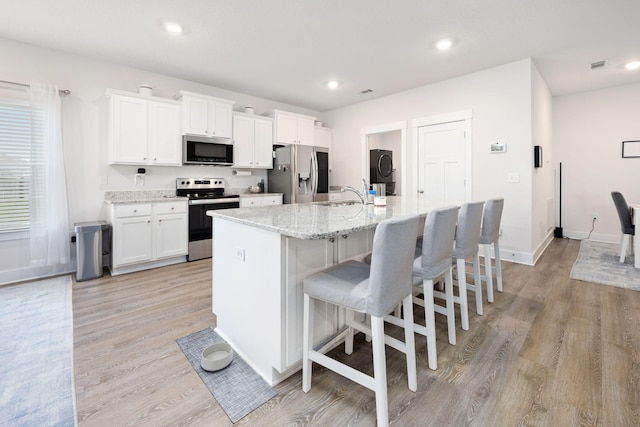 kitchen with an island with sink, appliances with stainless steel finishes, light hardwood / wood-style floors, and white cabinetry