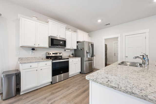 kitchen featuring light wood-type flooring, sink, white cabinets, stainless steel appliances, and light stone countertops