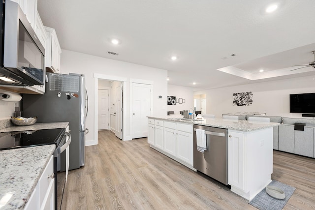 kitchen with appliances with stainless steel finishes, a kitchen island, light stone counters, and white cabinetry