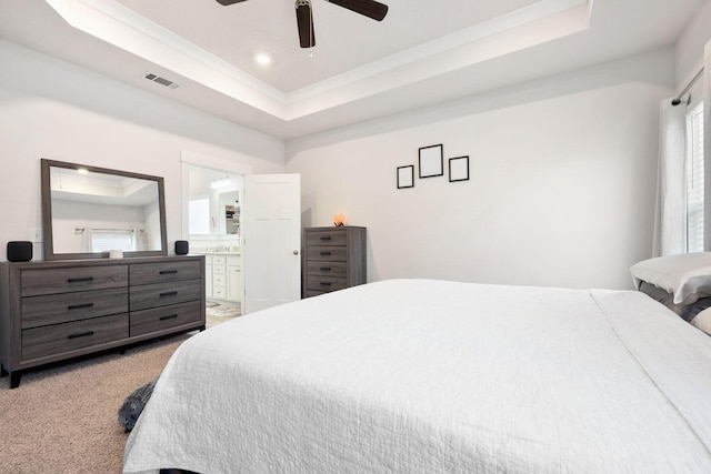 carpeted bedroom with ceiling fan, a tray ceiling, ensuite bathroom, and multiple windows